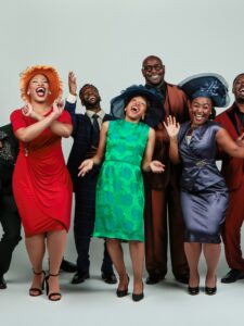 Group of men and women dressed in suits, fancy dresses and hats laughing and having fun