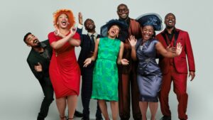 Group of men and women dressed in suits, fancy dresses and hats laughing and having fun