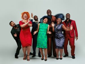 Group of men and women dressed in suits, fancy dresses and hats laughing and having fun