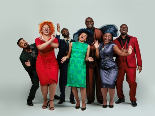 Group of men and women dressed in suits, fancy dresses and hats laughing and having fun