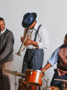 Three men playing musical instruments - piano, trumpet and drums in 1950s attire