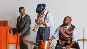 Three men playing musical instruments - piano, trumpet and drums in 1950s attire