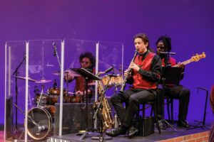 Three piece band playing in front of purple backgraound